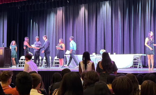 Students receive a certificate and handshake while being inducted.